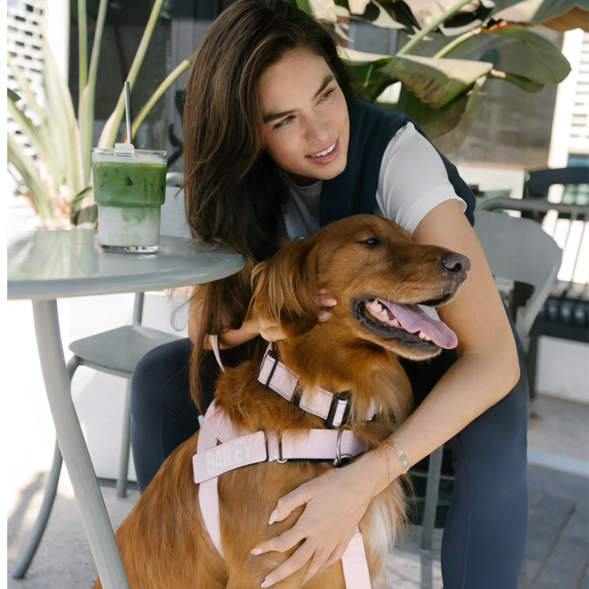 Woman hugging a golden retriever wearing the Sakura harness with a custom name patch at a cafe